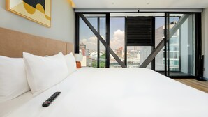 A modern hotel room with a large bed, a remote control, and a city view through floor-to-ceiling windows. - w* | Stunning 1BR w/ AC in the Heart of Roma Sur (Ciudad de México)