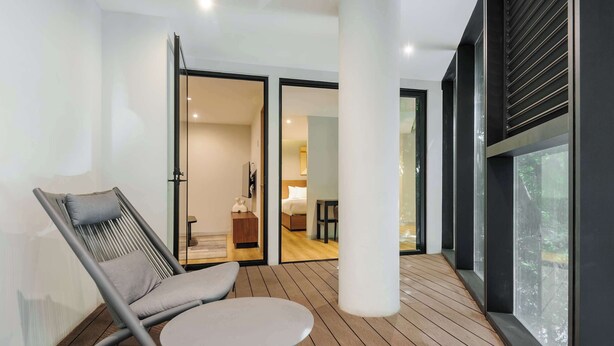 Ein modernes Zimmer mit Holzboden, einem grauen Sessel, einem kleinen runden Tisch und einem großen Fenster.