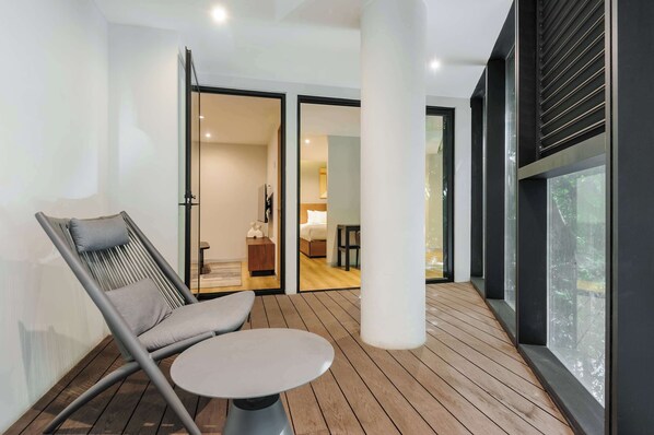 Ein modernes Zimmer mit Holzboden, einem grauen Sessel, einem kleinen runden Tisch und einem großen Fenster.