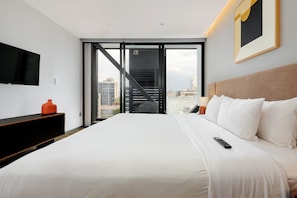 A modern hotel room with a large bed, a flat-screen TV mounted on the wall, and a city view through a large window. - w* | Deluxe 1BR w/ AC in the Heart of Roma Sur (Ciudad de México)