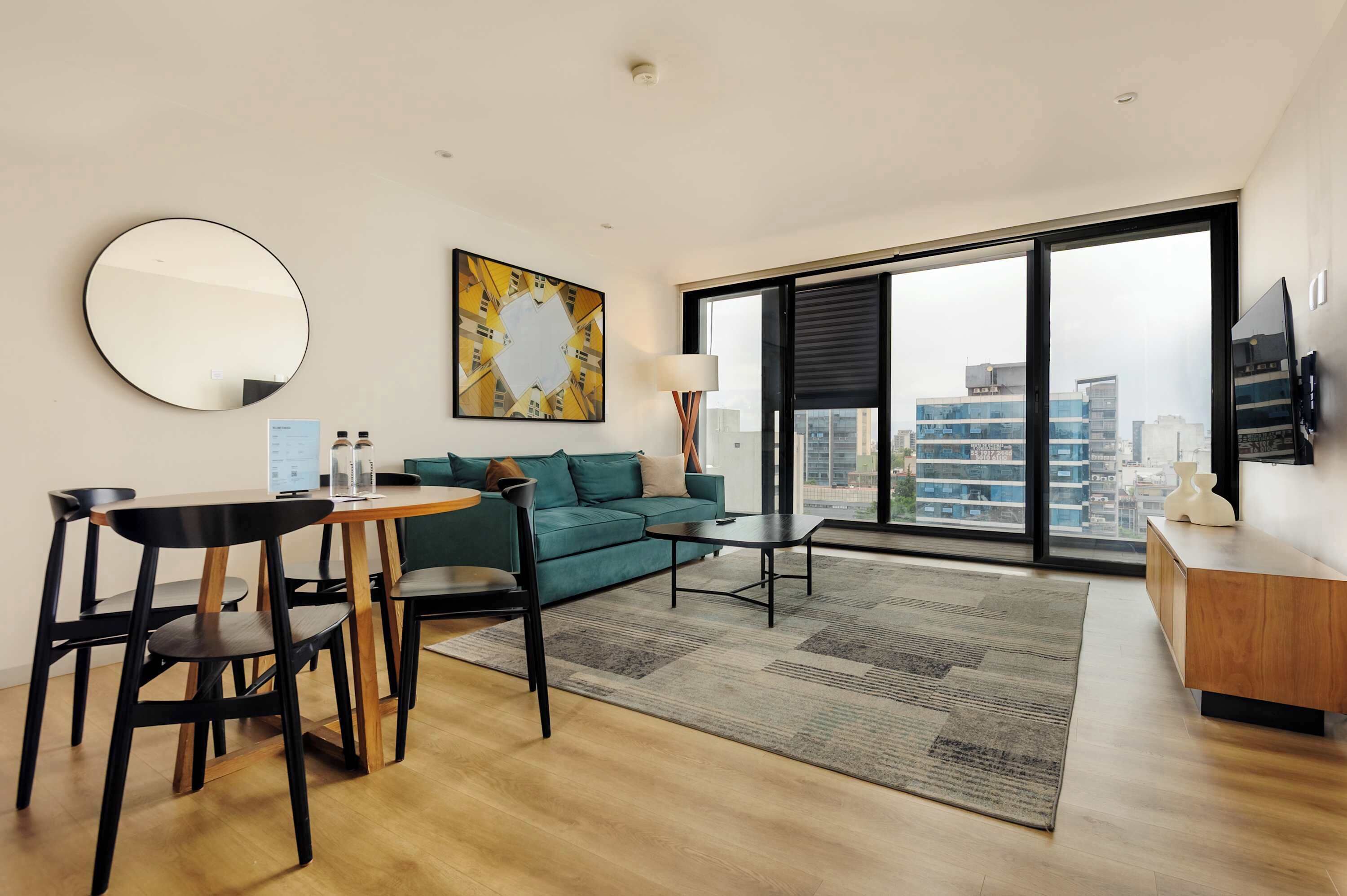 Un salon moderne avec un grand miroir rond, un canapé vert, une table basse et une vue sur la ville grâce à de grandes fenêtres.
