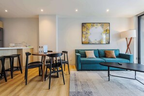 Ein modernes Wohnzimmer mit einem türkisgrünen Sofa, schwarzen Stühlen, einem Couchtisch und einem Gemälde an der Wand.
