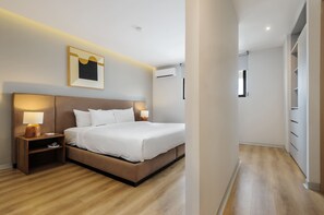 Ein modernes Hotelzimmer mit einem großen Bett, Nachttischlampen, einem gerahmten Kunstwerk und einer Klimaanlage.