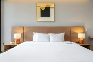 Ein Hotelzimmer mit einem großen Bett, zwei Nachttischen mit Lampen, einem Wandbild und einem Beistelltischchen mit Telefon.