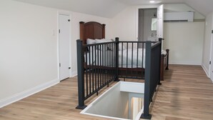 Un dormitorio con cama de madera, baranda de metal negro, puerta blanca y unidad de aire acondicionado blanca.