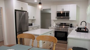 Una cocina moderna con armarios blancos, electrodomésticos de acero inoxidable y una mesa de comedor de madera con sillas.