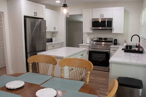 A modern kitchen with white cabinets, stainless steel appliances, and a wooden dining table with chairs.