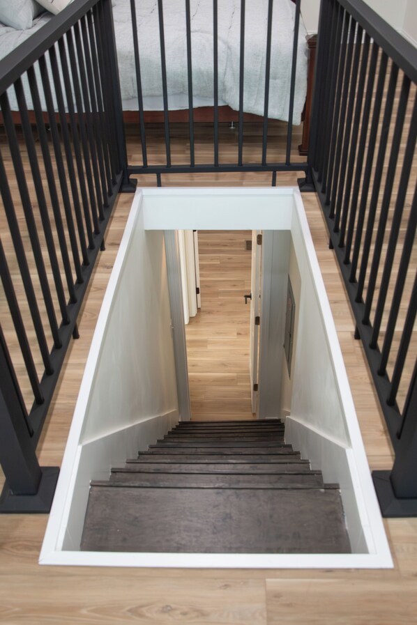 A modern staircase with black railings and wooden steps leading to a bedroom with a white bed and a wooden floor.