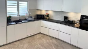 A modern kitchen with white cabinets, a black countertop, a sink, a microwave, and a coffee maker. - Front Street Gem - Steps to Beach & Shopping (Philipsburg)