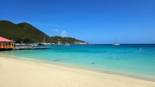A beach with clear turquoise water, a red-roofed building, and a lighthouse in the distance. - Front Street Gem - Steps to Beach & Shopping (Philipsburg)