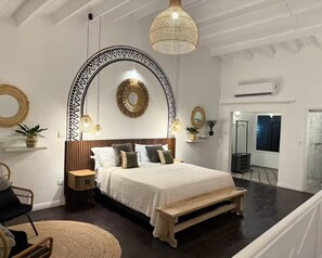 Ein Schlafzimmer mit Bett, Nachttischen, einer Pendelleuchte und einem Spiegel an der Wand.