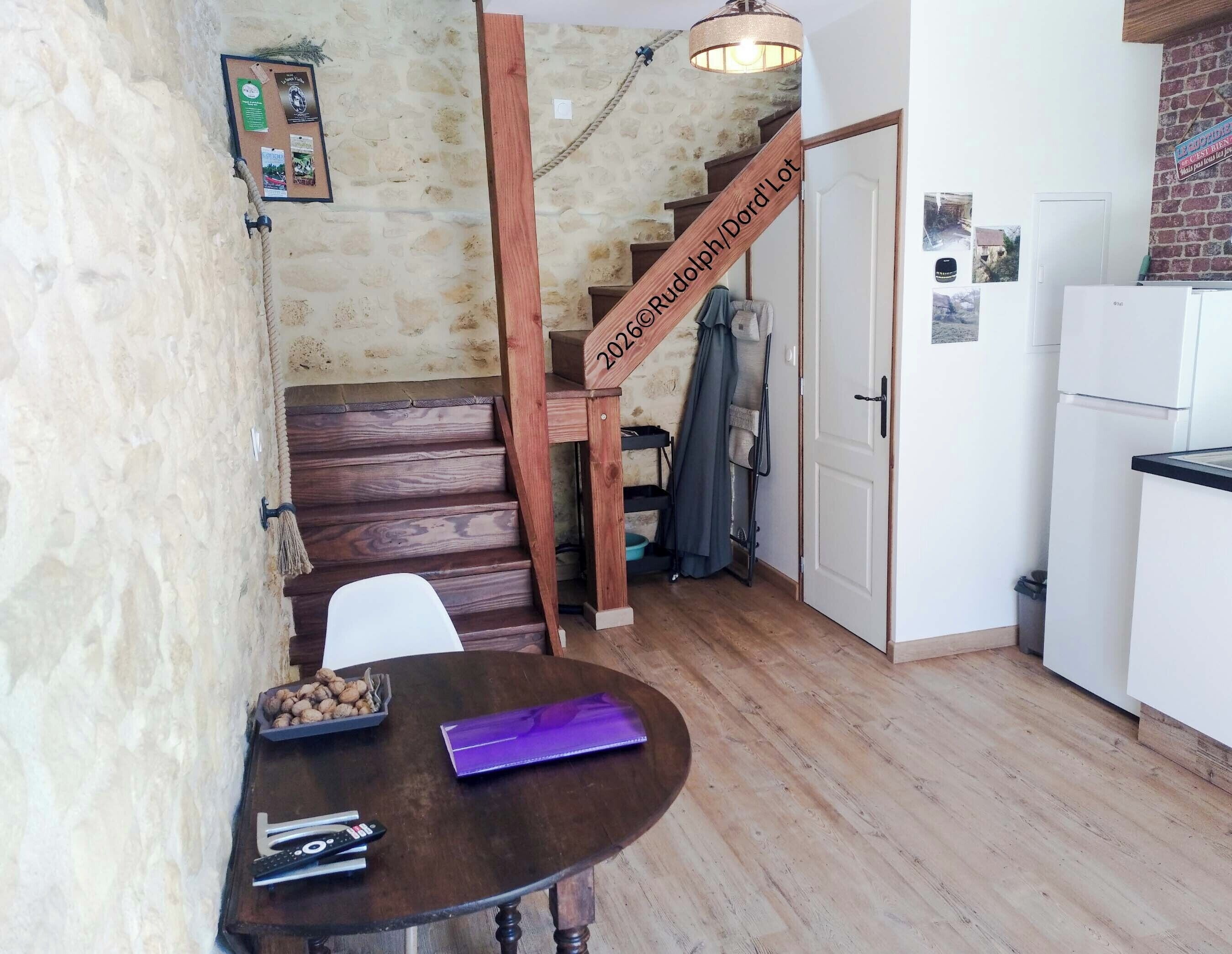 A kitchen with a wooden staircase, a dining table with a basket of nuts, and a refrigerator.
