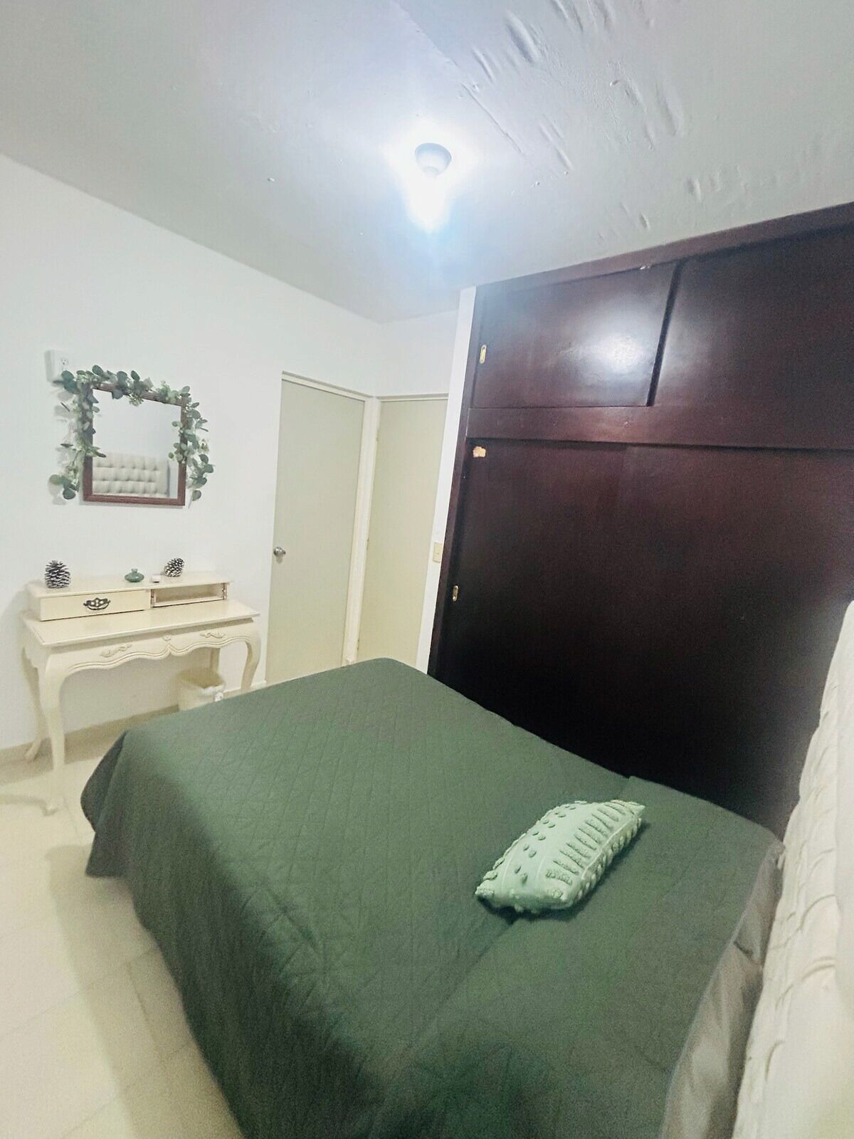 Um quarto com cama, cômoda, espelho com grinalda e porta.