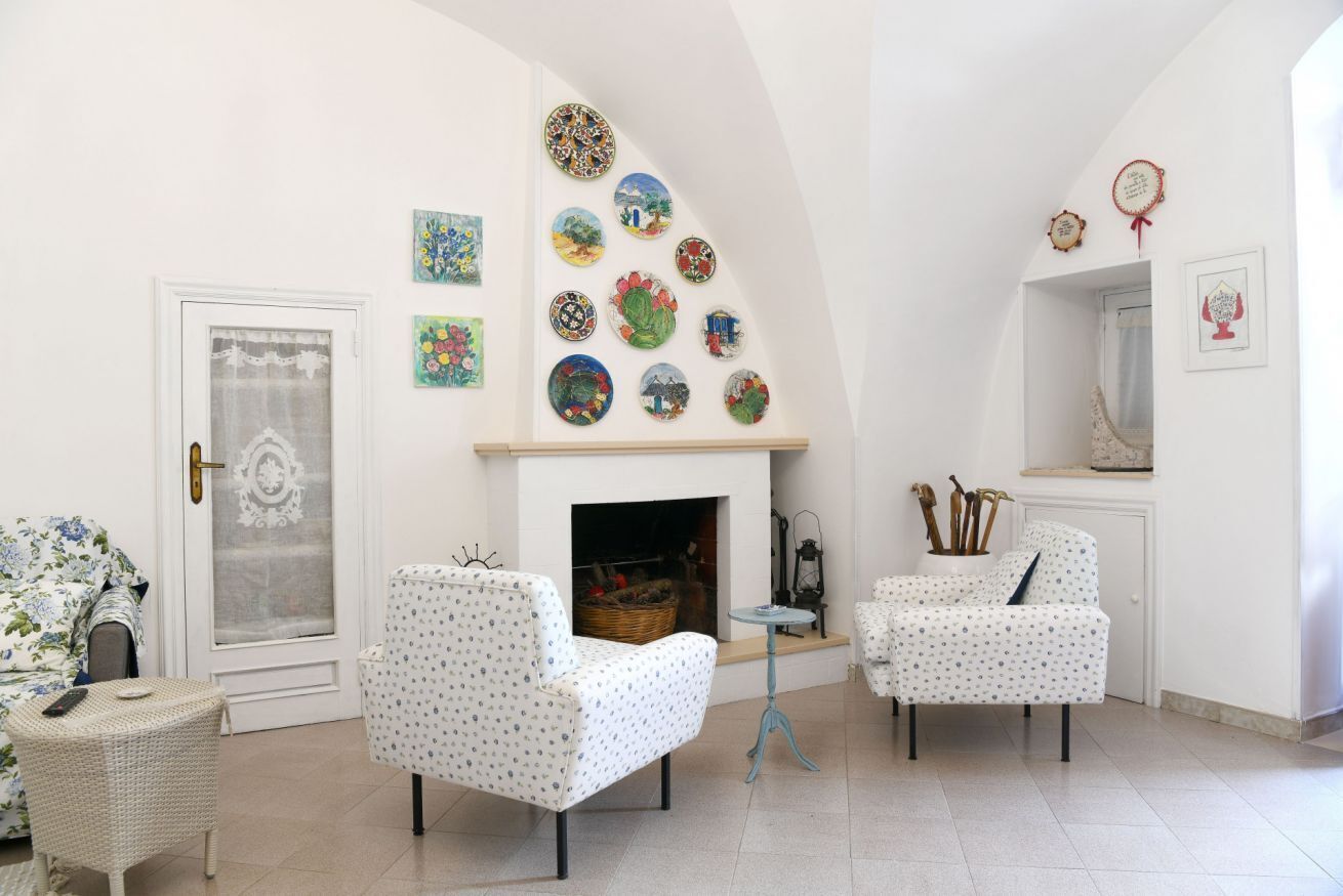A room with two white armchairs, a small table, a fireplace, and a wall decorated with colorful plates.