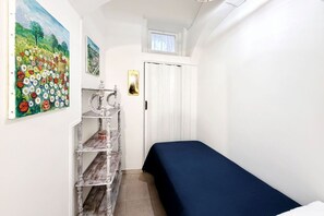 A small, narrow room with a bed, a shelf with items, a door, and a painting on the wall. - Agata' House, nel fascino del borgo (Cisternino)