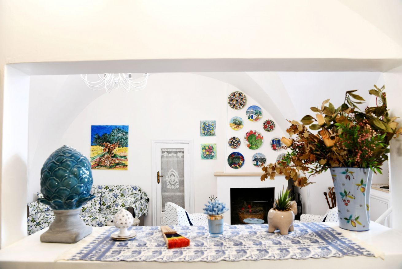 Een kamer met een witte muur, een blauw-wit geruit tafelkleed, een vaas met gedroogde bloemen, een blauwe keramieken wereldbol en een schilderij van een landschap.