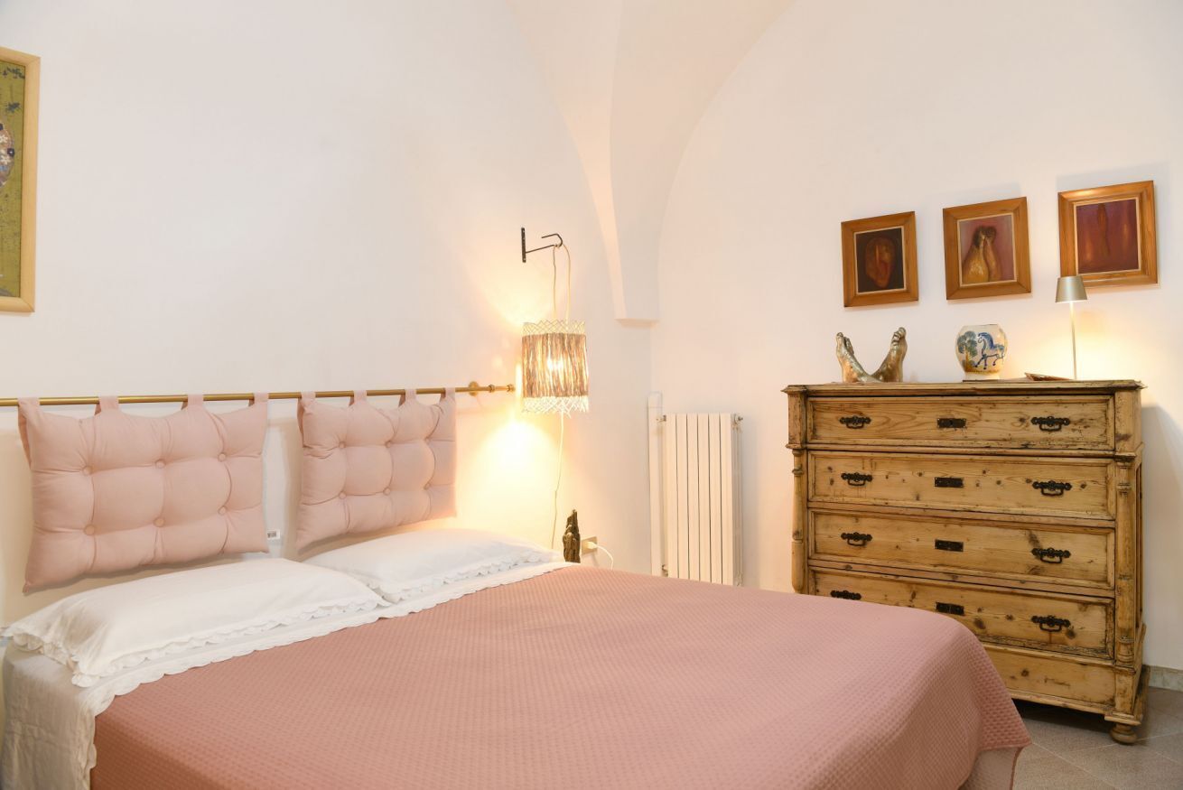 Une chambre à coucher comprenant un lit, une commode, des œuvres d’art accrochées au mur et une lampe fixée au mur.