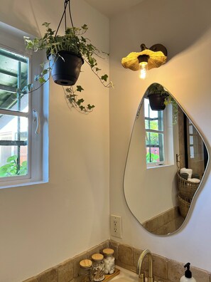 Ein Badezimmer mit großem Spiegel, einem Topfpflanzen, einer Pendelleuchte und einem Fenster.