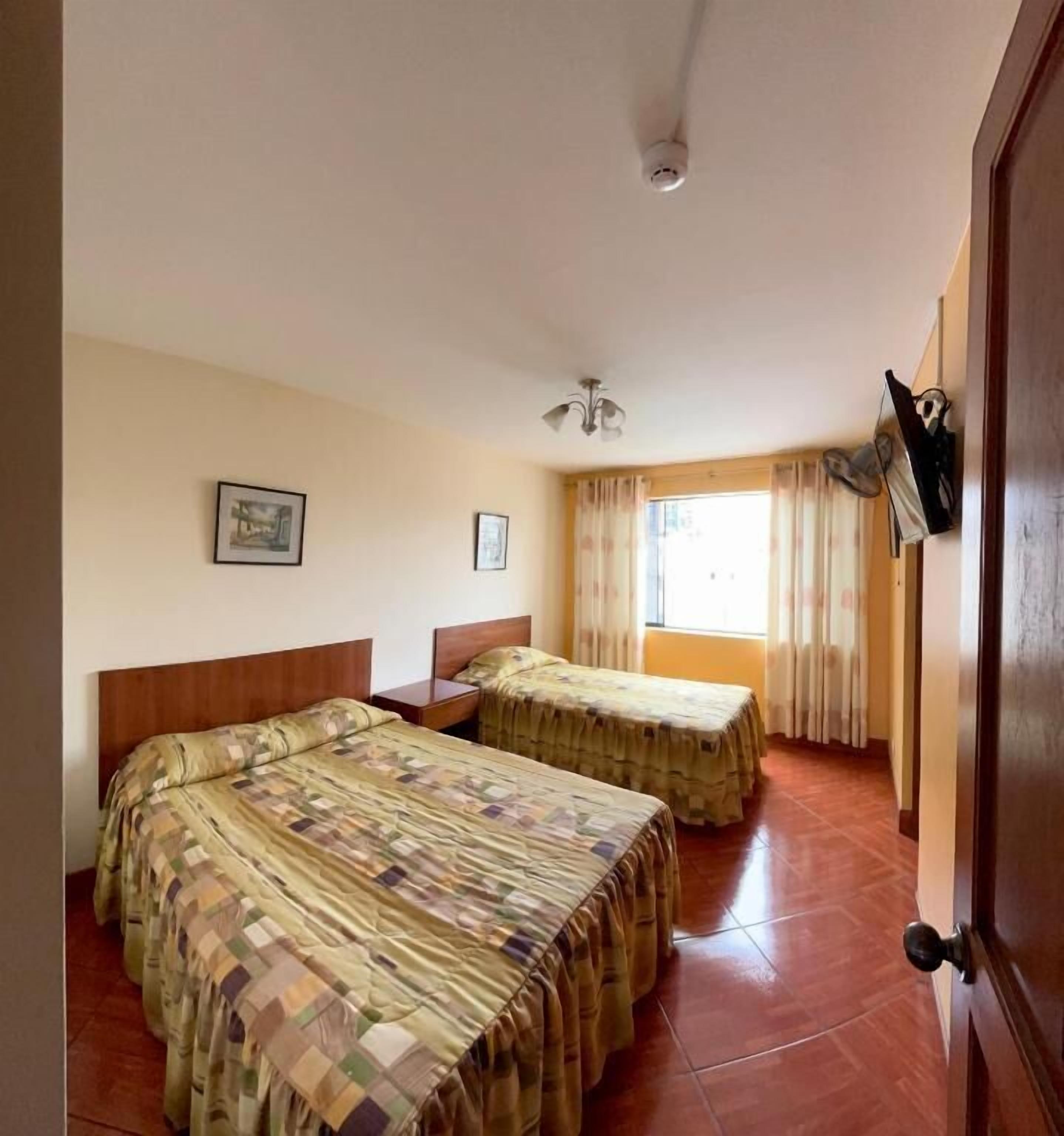 A room with two beds, a ceiling fan, a window with curtains, and a door with a handle.