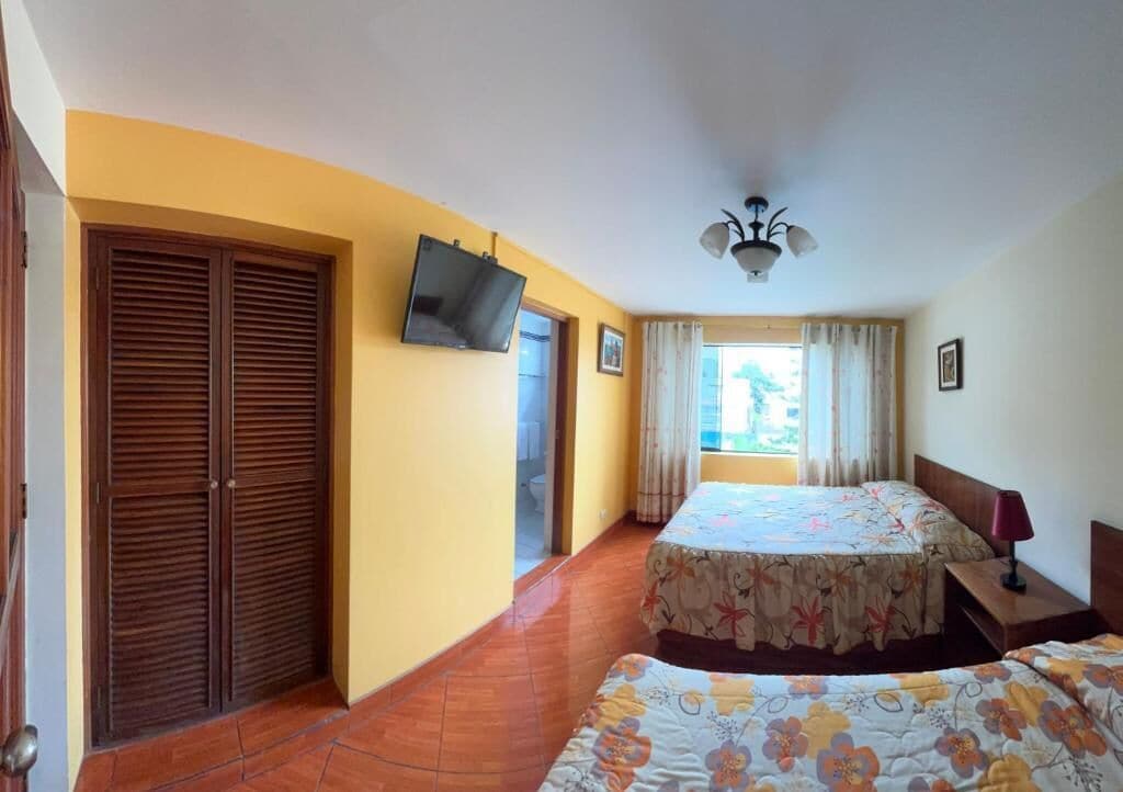 A hotel room with a bed, a TV mounted on the wall, a ceiling fan, and a window with curtains.
