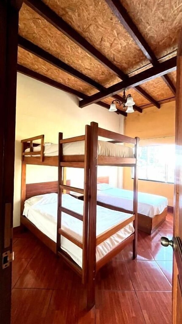 A room with a bunk bed, wooden ceiling beams, a window, and a door. - Hotel Nirvana Miraflores (Lima)