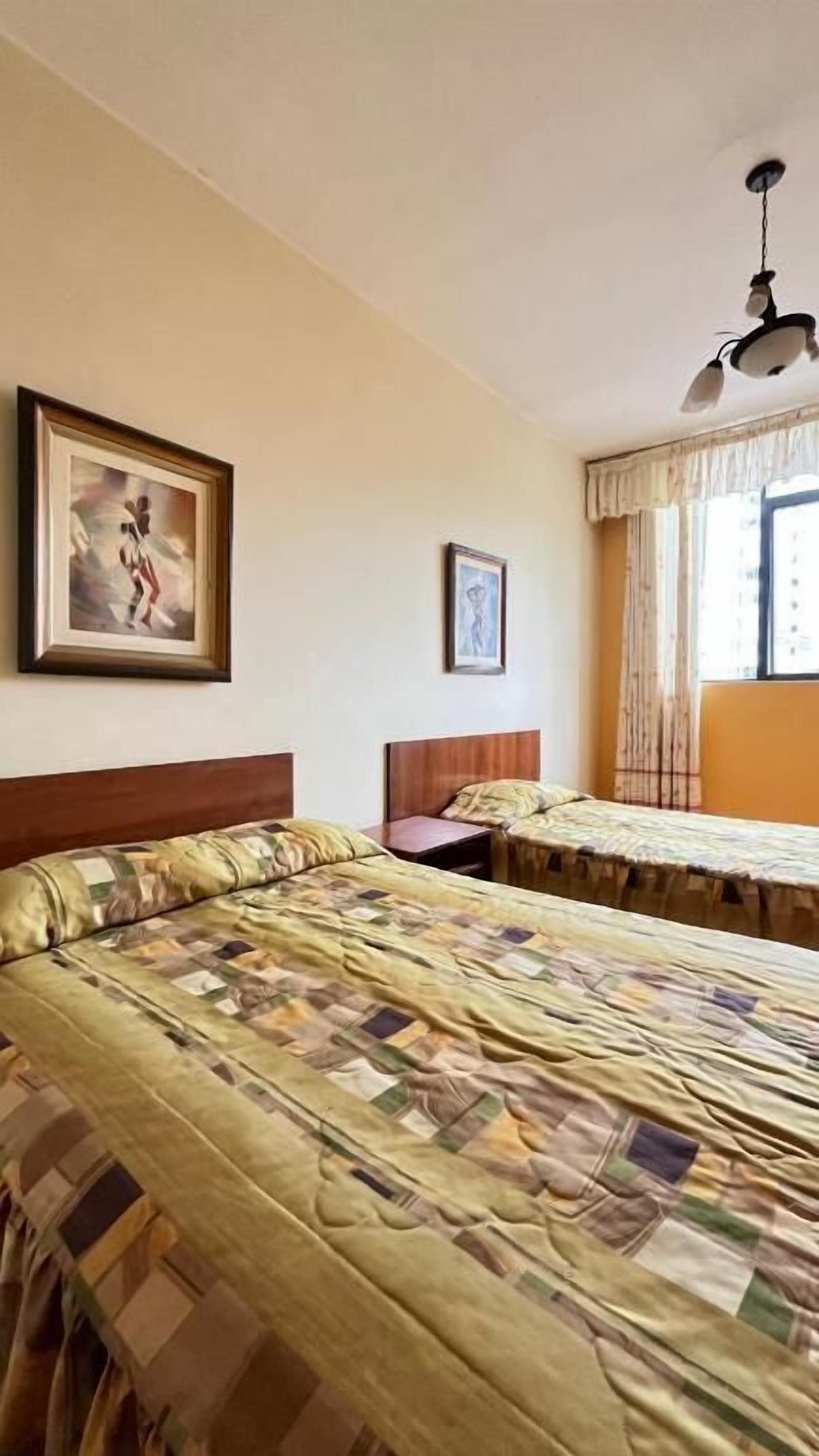 A hotel room with two beds, a wooden headboard, a ceiling fan, and a window with curtains.