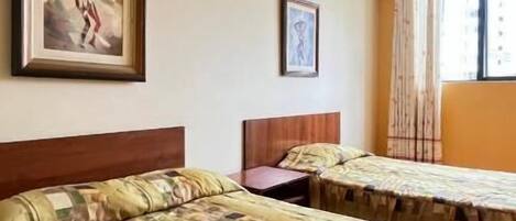 A hotel room with two beds, a wooden headboard, a ceiling fan, and a window with curtains.
