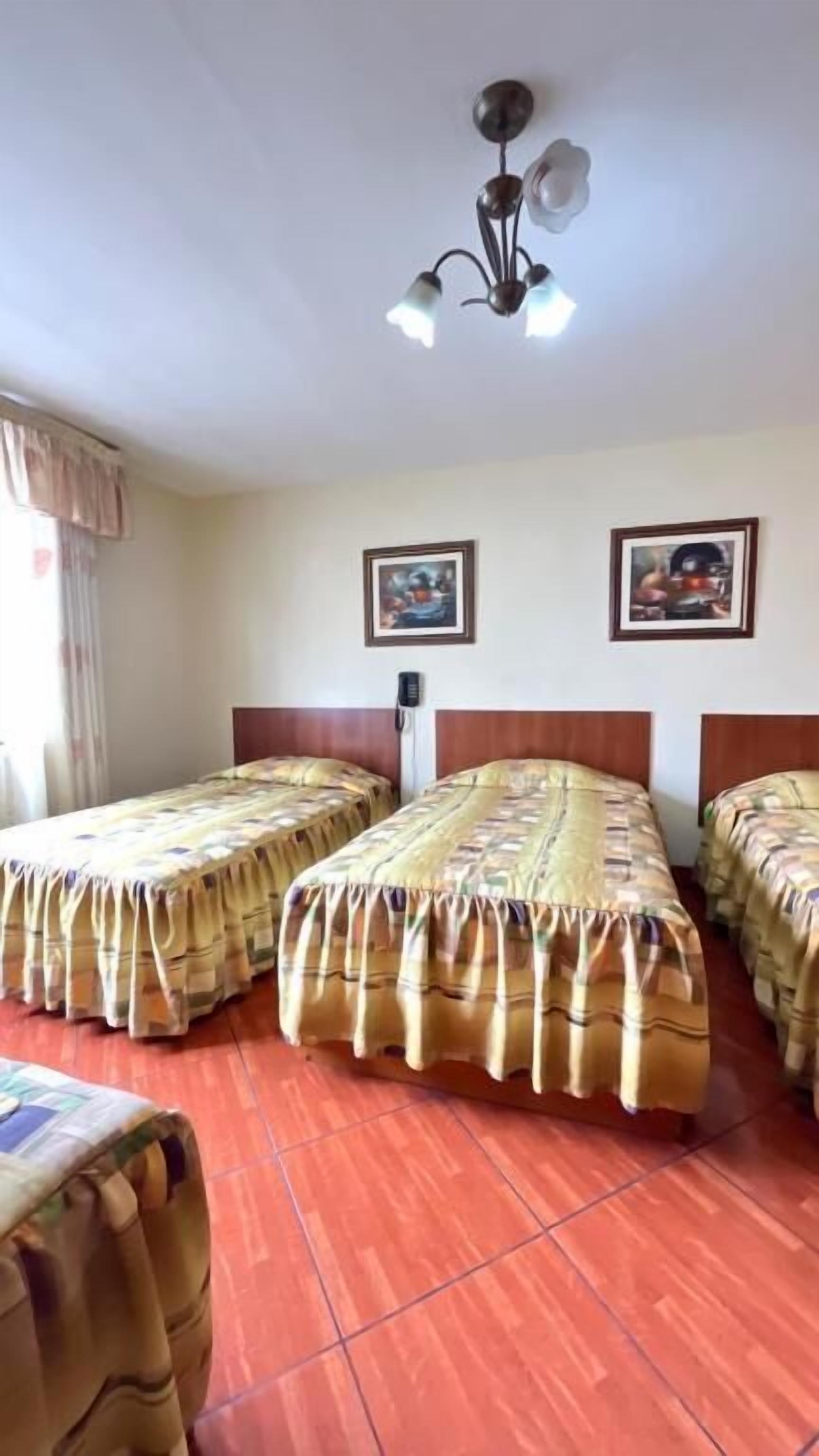 Une chambre d’hôtel avec deux lits, un ventilateur de plafond et deux tableaux encadrés au mur.