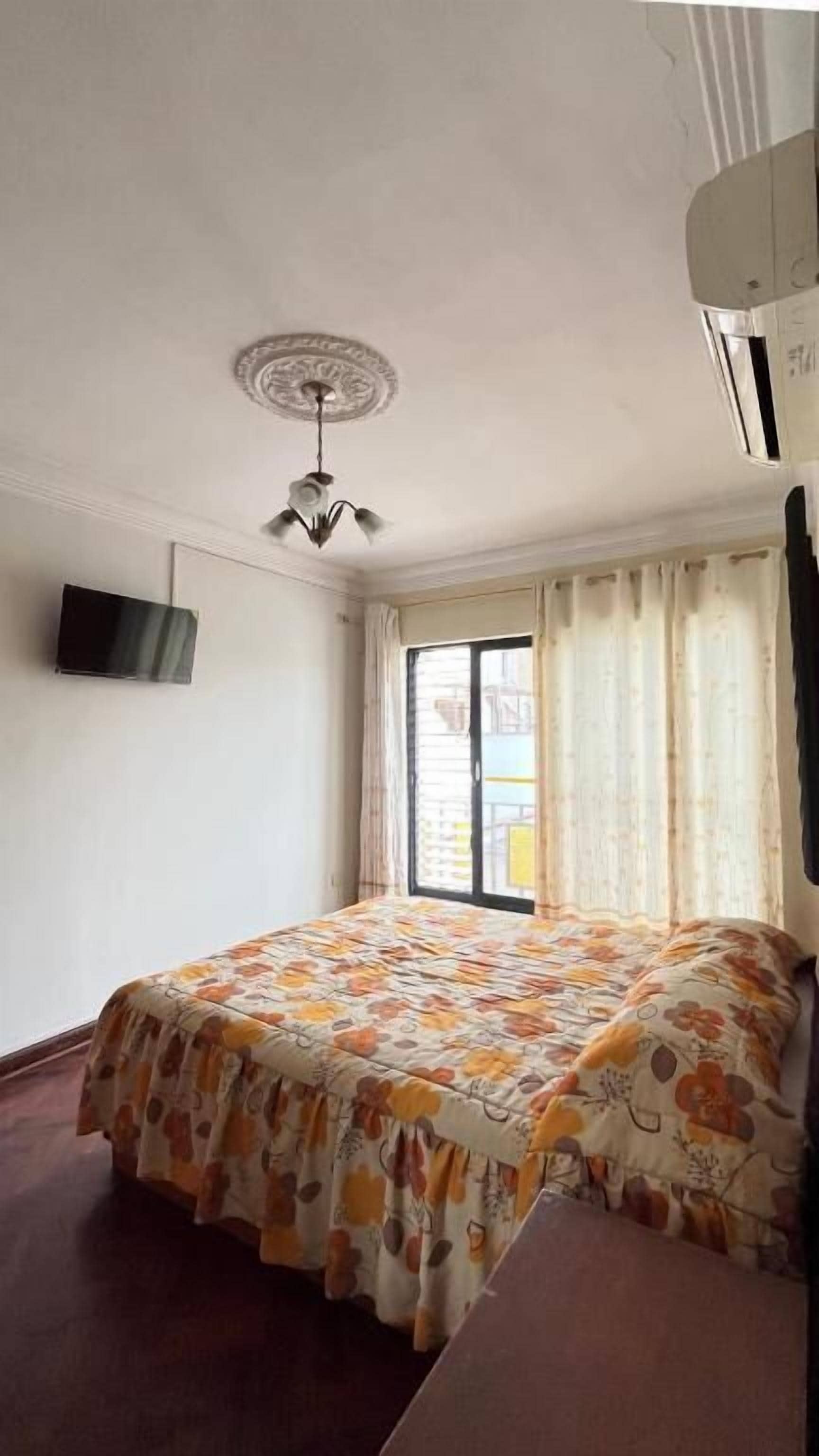 A room with a bed, a ceiling fan, a flat-screen TV, and a window with curtains.