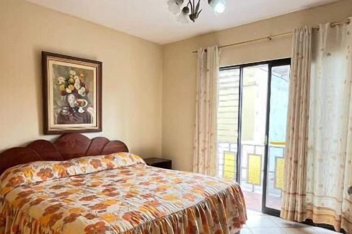 Un dormitorio con cama, candelabro, ventana con cortinas y puerta.