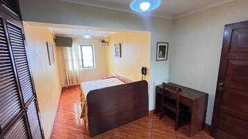 Un dormitorio con cama, escritorio, silla, ventana y puerta.