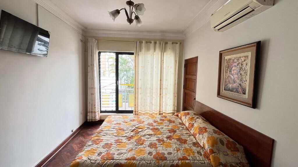 Un dormitorio con una cama, un televisor, un cuadro y una ventana con cortinas.