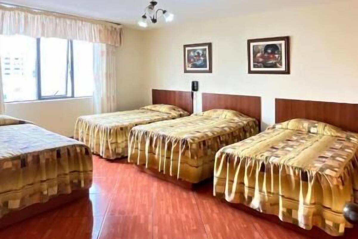 Una habitación con una cama grande, dos camas más pequeñas, una ventana con cortinas y una lámpara en el techo.