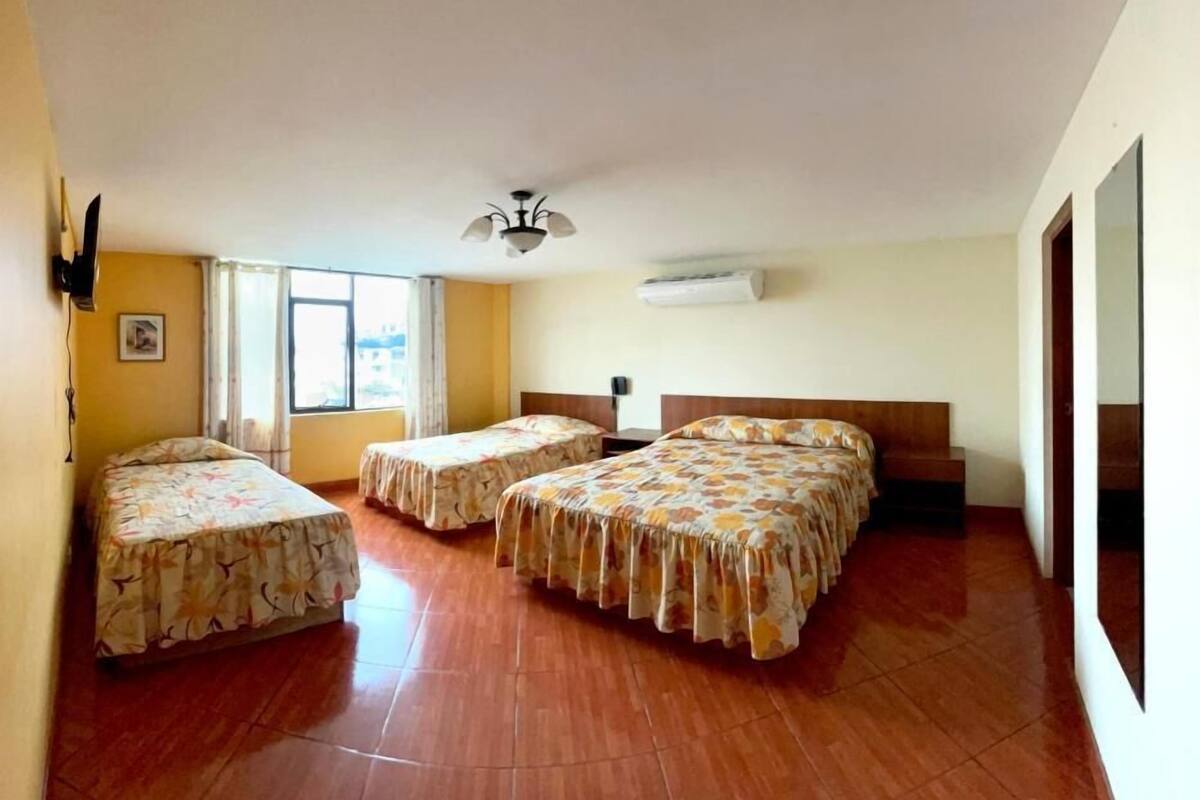 Habitación de hotel con tres camas, ventilador de techo, aire acondicionado y un ventanal grande.