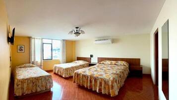 Habitación de hotel con tres camas, ventilador de techo, aire acondicionado y un ventanal grande.