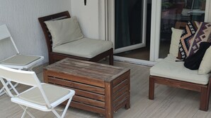 An outdoor patio with a striped awning, a wooden coffee table, two white folding chairs, and a cushioned chair with a patterned pillow. - Peaceful 1-bedroom apartment with AC in wonderful Beograd (Beograd)