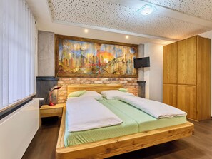 A bedroom with a wooden bed, a brick wall, a painting, a TV, and a wardrobe. - Roky - Dolní náměstí by Interhome (Rokytnice nad Jizerou)