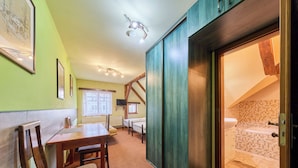 A room with a wooden table, chairs, a bed, and a bathroom with a tiled wall. - Roky - Dolní náměstí by Interhome (Rokytnice nad Jizerou)