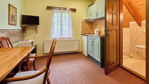A compact kitchen with a dining area, a television, and a wooden door leading to a bathroom. - Roky - Dolní náměstí by Interhome (Rokytnice nad Jizerou)