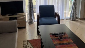 Una sala de estar con televisor, sofá, mesa de centro y una silla.