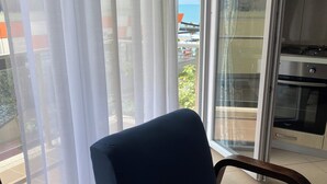 A room with a blue chair, a glass door leading to a balcony, and a kitchen area. - Lis - Holiday Apartments (Lezhë County)