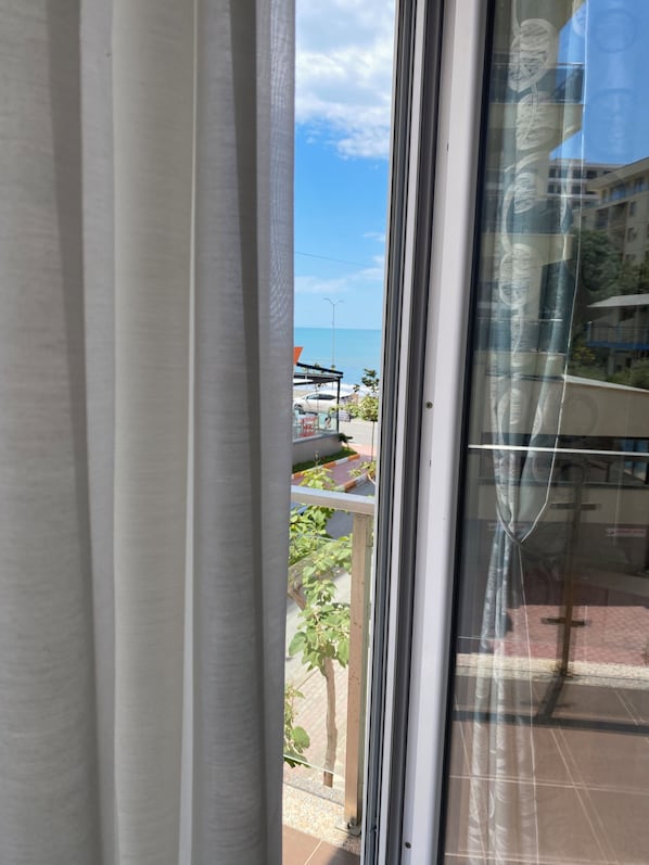 A view through a window with a curtain, a clear sky, and a glimpse of a building and greenery outside.