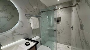 Ein modernes Badezimmer mit Waschtisch aus Marmor, einer Duschkabine aus Glas und einer Toilette.