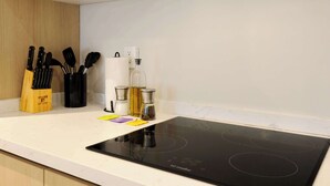 Eine Küche mit einem schwarzen Induktionskochfeld, einem Messerblock, einem Gewürzregal und einer weißen Arbeitsplatte.