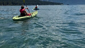 Dos kayakistas en un lago tranquilo con cielos despejados y montañas a lo lejos.
