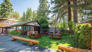 Una cabaña con chimenea de piedra, mesas de picnic y un rincón con bancos de madera.