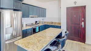 A kitchen with a granite countertop, stainless steel appliances, blue cabinets, and a dark wooden door. - Luxurious Mountain-view Apartment Close to the sea With Rooftop Sunset Views (Cabo San Lucas)