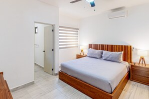 Ein modernes Schlafzimmer mit einem hölzernen Bettgestell, zwei Nachttischen mit Lampen, einem Deckenventilator und einem Fenster mit Jalousien.