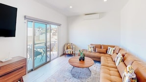 A modern living room with a sofa, a coffee table, a TV, and a sliding glass door leading to an outdoor area. - Luxurious Mountain-view Apartment Close to the sea With Rooftop Sunset Views (Cabo San Lucas)