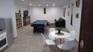 Une pièce comprenant une table de billard, un canapé, un téléviseur et un coin repas avec des chaises.
